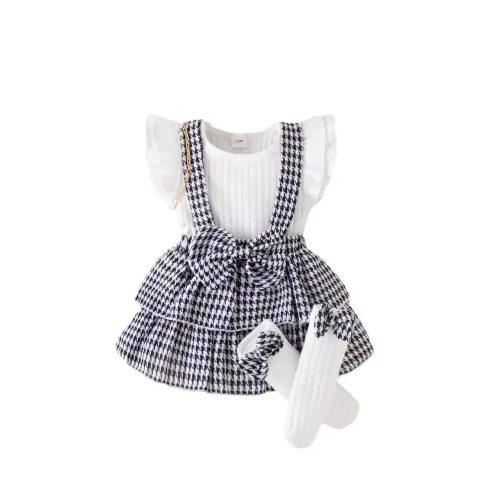Toddler girl houndstooth suspender skirt set with ribbed white top, ruffled sleeves, pleated front, and black & white houndstooth skirt with waist bow, displayed for catalog