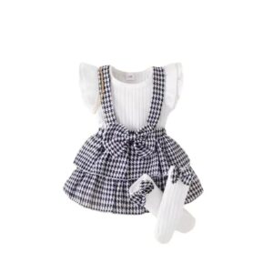 Toddler girl houndstooth suspender skirt set with ribbed white top, ruffled sleeves, pleated front, and black & white houndstooth skirt with waist bow, displayed for catalog