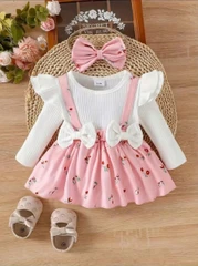 Baby girl outfit set with cream ribbed top, floral suspender skirt, matching headband bow, and beige shoes with bows, arranged on wooden surface.