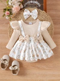 Baby girl outfit set with cream ribbed top, floral suspender skirt, matching headband bow, and beige shoes with bows, arranged on wooden surface.