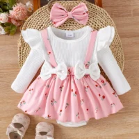 Baby girl outfit set with cream ribbed top, floral suspender skirt, matching headband bow, and beige shoes with bows, arranged on wooden surface.