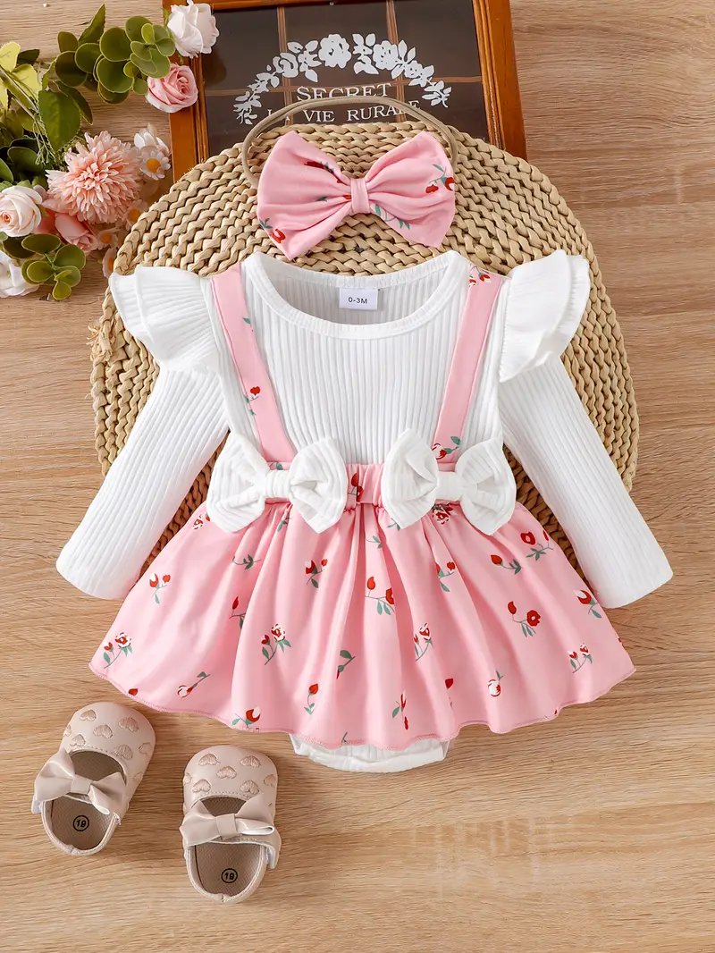 Baby girl outfit set with cream ribbed top, floral suspender skirt, matching headband bow, and beige shoes with bows, arranged on wooden surface.
