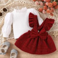 Baby girl red pinafore dress set with sparkly red pinafore, ruffled straps, large bow, and white ribbed top, displayed for catalog.