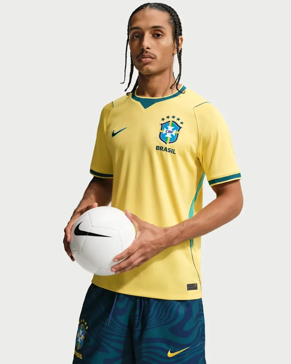 CBF+M+NK+DF+JSY+SS+STAD+HM A man with braided hair modeling the official yellow 2026 Brazil national football team home jersey while holding a white football, as seen in the product