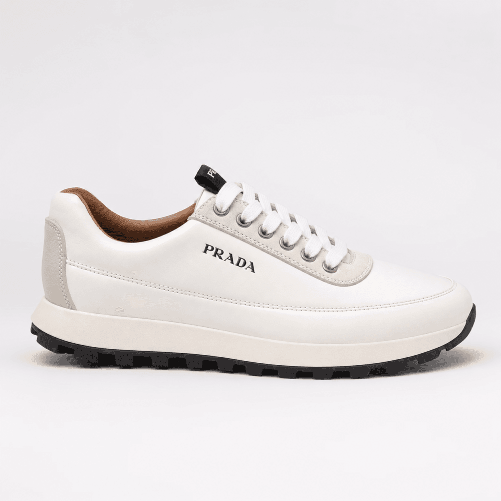 Lateral profile view of a luxury Prada low-top sneaker in white leather with a black treaded outsole — Premium Men's Designer Footwear Rwanda.